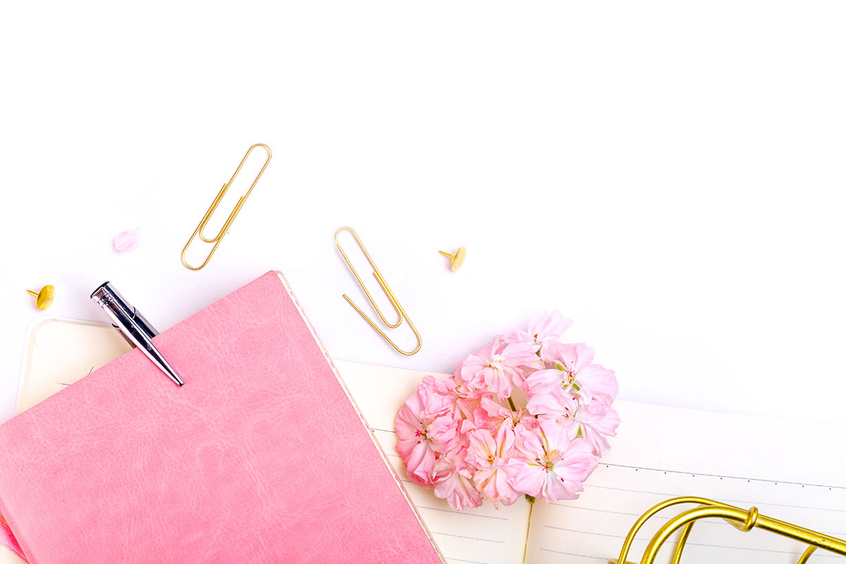A pink notebook with flowers and a pen on a white background.