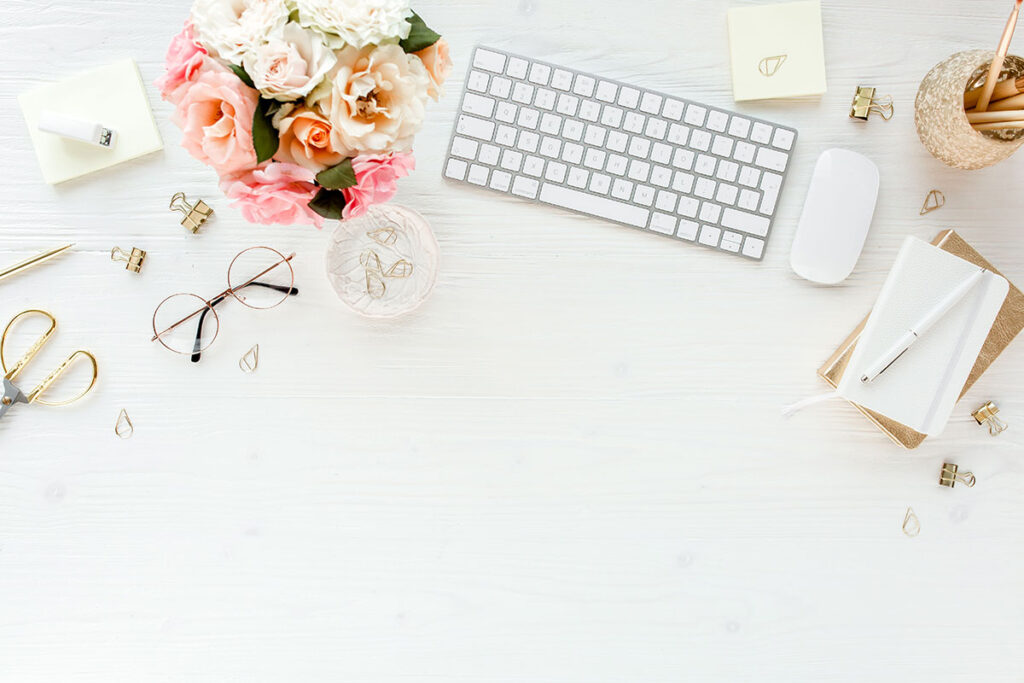 A white desk with a vase of flowers, a keyboard, and other office supplies.